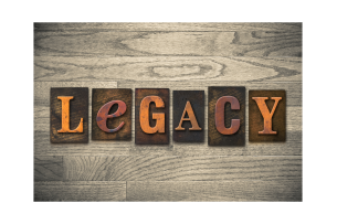 Six blocks with the letters spelling "LEGACY," in orange, atop a wooden table.